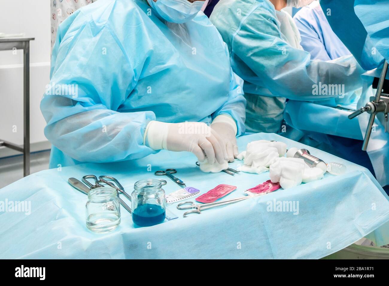 Strumenti chirurgici sterili e contenitori in vetro con soluzioni sul tavolo durante un intervento chirurgico. Sopra la tabella sono le mani di un chirurgo Foto Stock