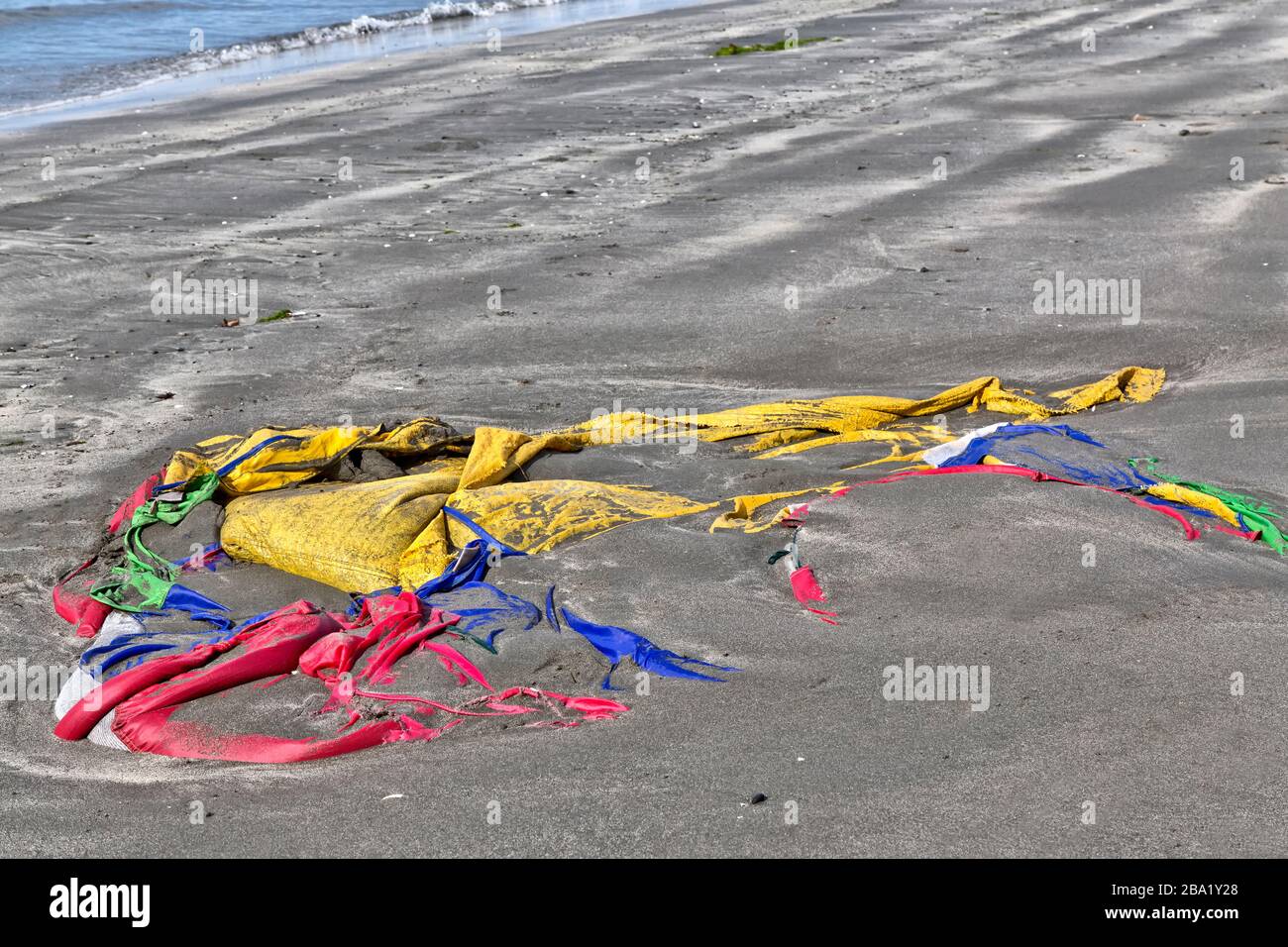 Marea in arrivo depositato colorato tenda poliestere lungo la spiaggia costiera. Foto Stock