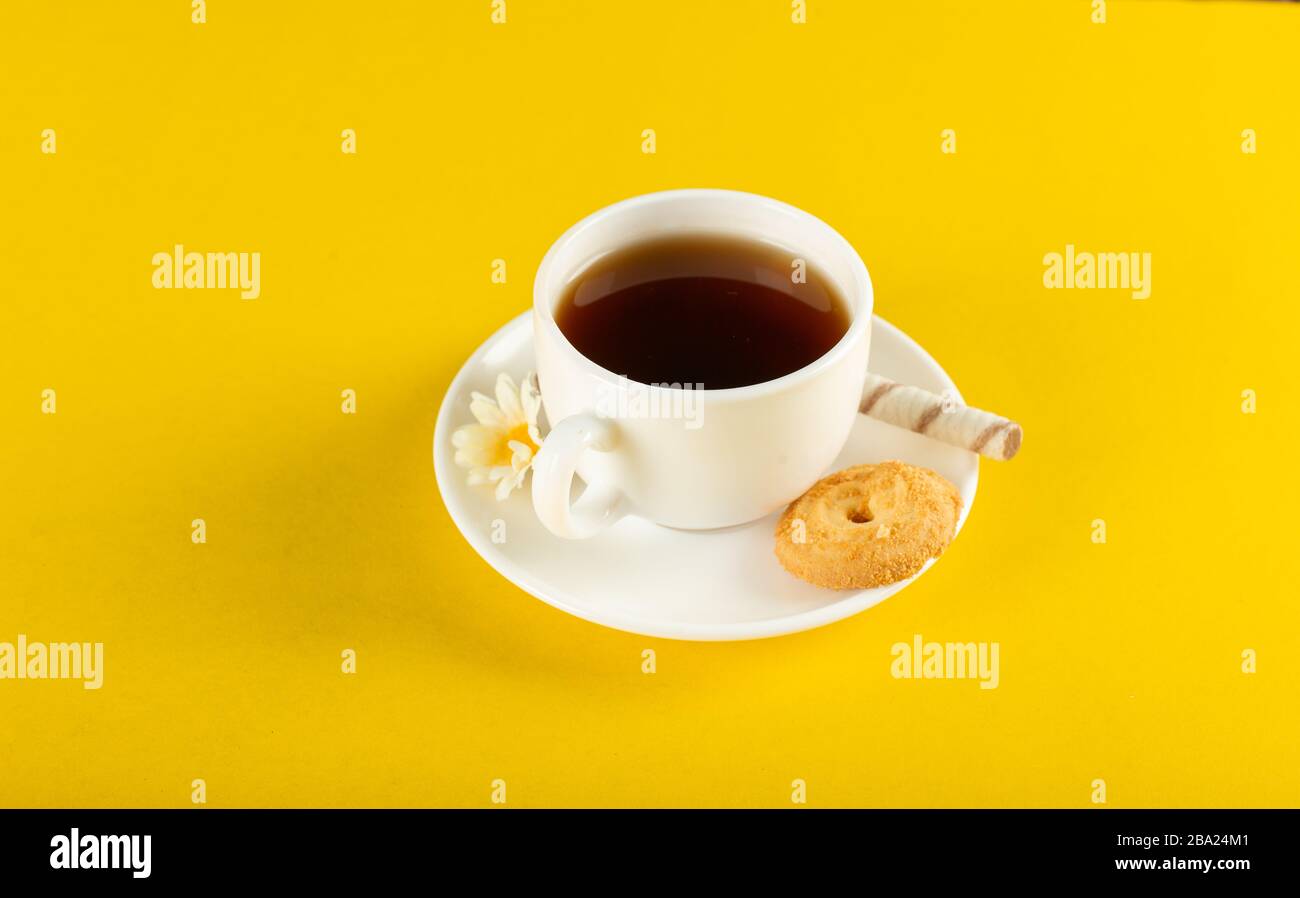 Una tazza di tè con biscotto su sfondo giallo Foto Stock