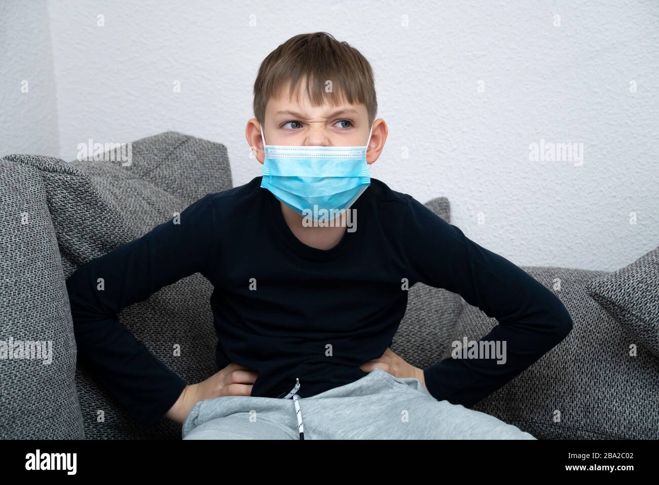 Il ragazzo arrabbiato offeso siede in una maschera a casa in quarantena. Primo piano. Epidemia di coronavirus COVID19. Bambino in quarantena a casa isolato. Autoisolamento Foto Stock