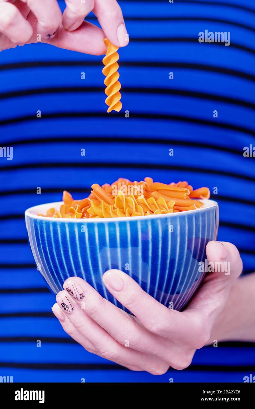 Ciotola per mani femminili con lenticchie di arancia fusilli su fondo a righe blu. Concetto di dieta e senza glutine Foto Stock