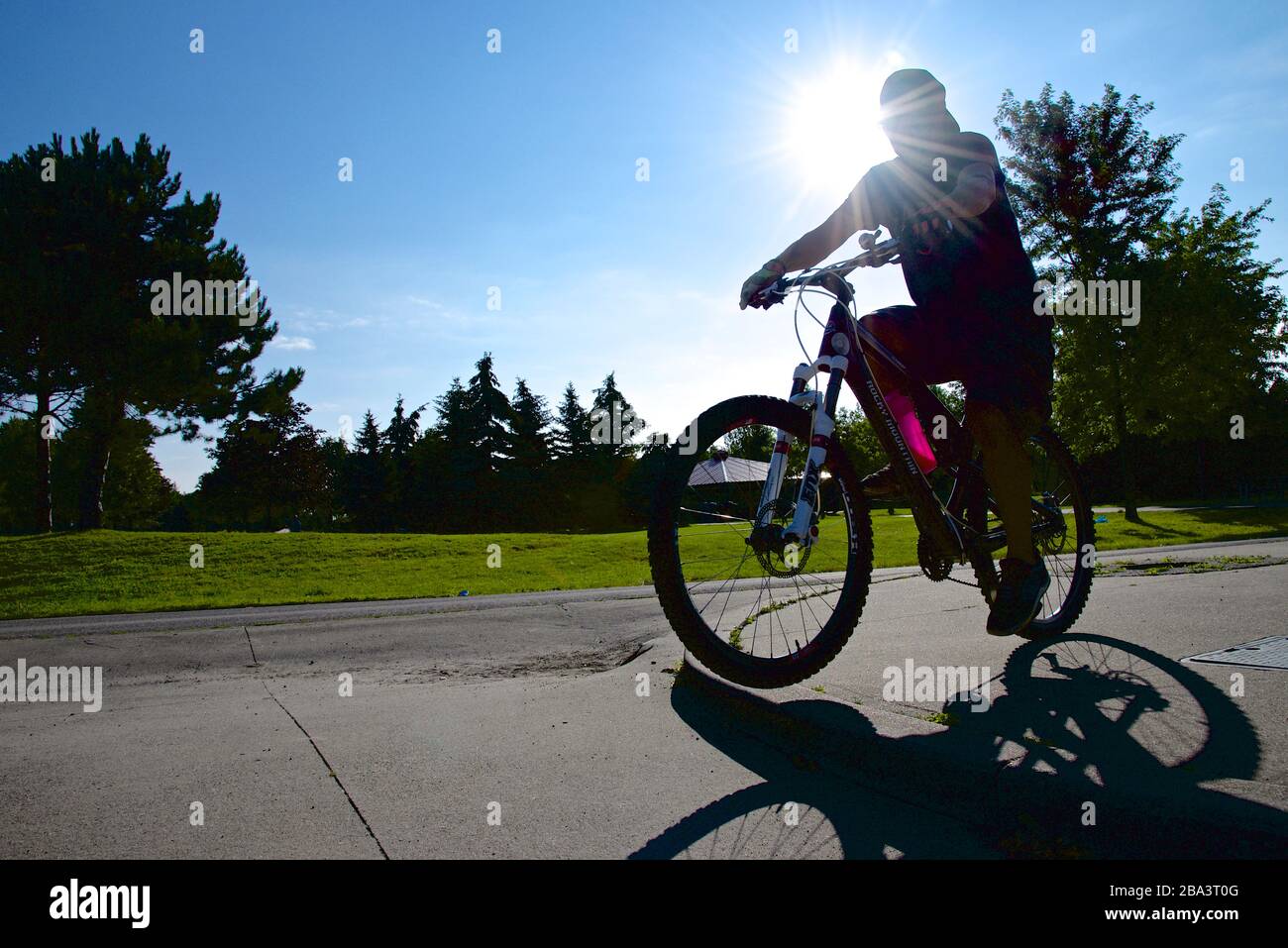 silhouette del mountain biker equitazione nel parco pubblico con lente di fioca Foto Stock