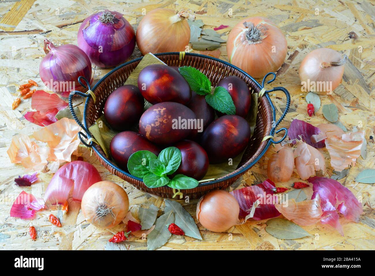 Uova di Pasqua in cesta di vimini e cipolla gialla e rossa, peperoni e basilico verde e foglie di balsamo al limone su sfondo di legno, vista ad angolo Foto Stock