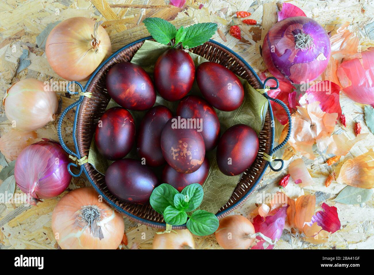 Uova di Pasqua in cesta di vimini e cipolla gialla e rossa, peperoni e basilico verde e foglie di balsamo al limone su sfondo di legno, vista dall'alto Foto Stock