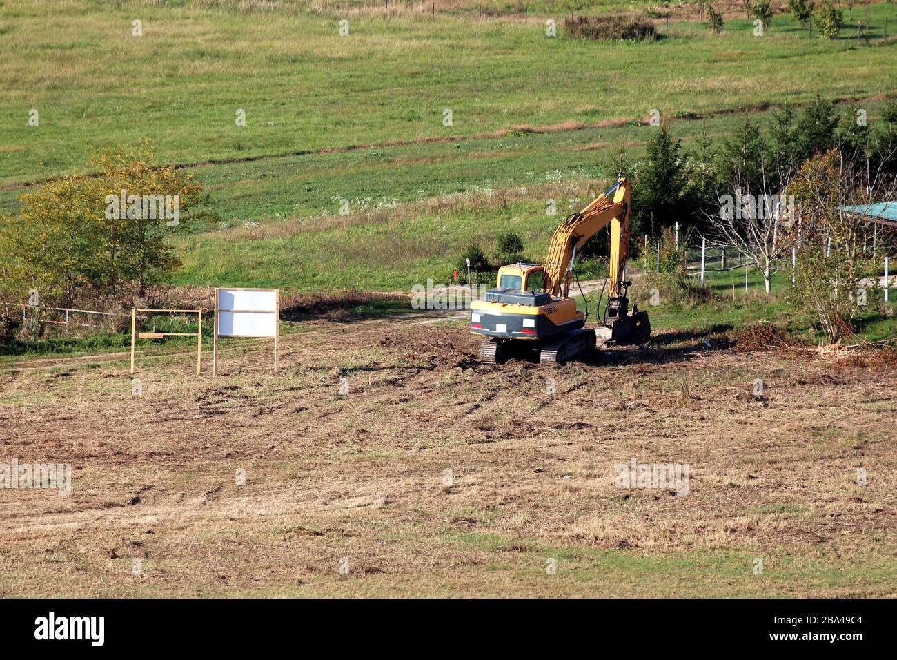 Sito di costruzione locale appena appiattito e pulito con un solo escavatore parcheggiato dopo il lavoro circondato da erba parzialmente asciutta e piccoli alberi Foto Stock