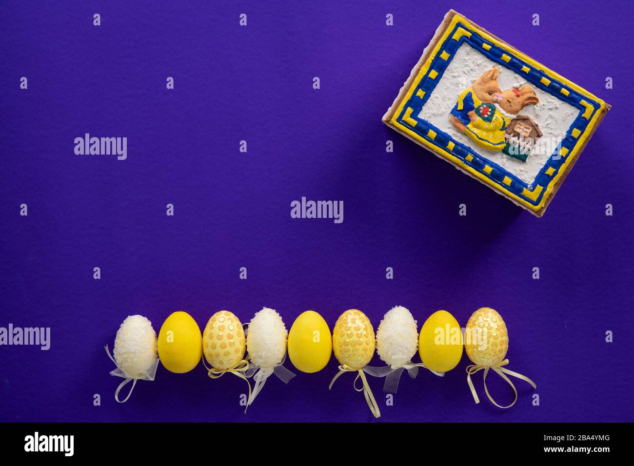 Uova di pasqua bianche e gialle e una scatola di coniglietto chiusa su una superficie viola scura Foto Stock