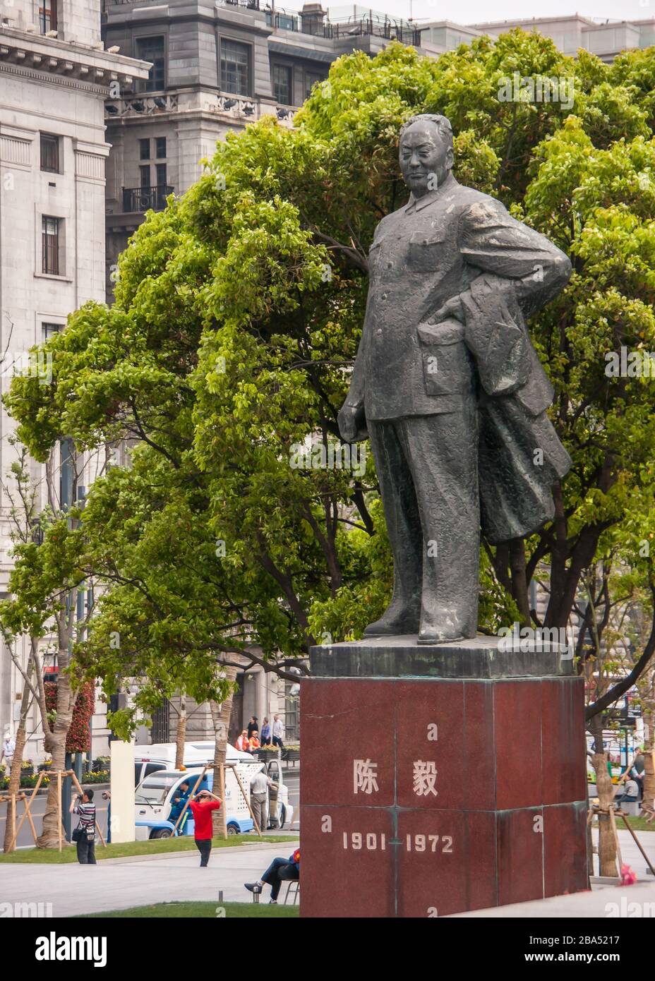 Shanghai, Cina - 4 maggio 2010: Massiccia statua grigia sul piedistallo rosso di Chen Yi, primo sindaco, un uomo, con fogliame verde alle sue spalle. Parti dell'edificio f Foto Stock