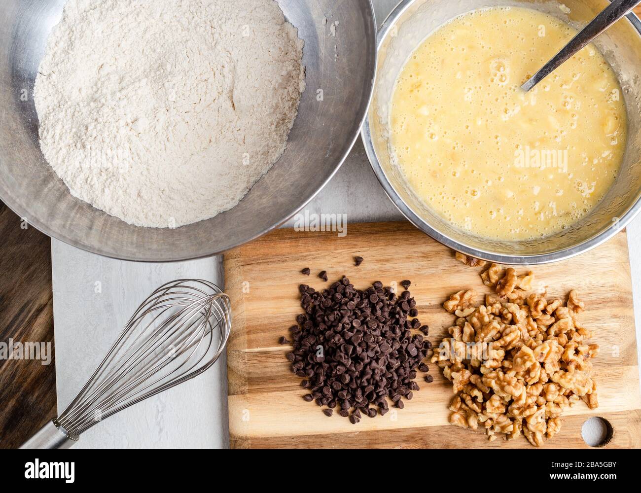 Preparazione del pane alla banana in ciotole di miscelazione con noci e patatine di cioccolato, vista dall'alto Foto Stock