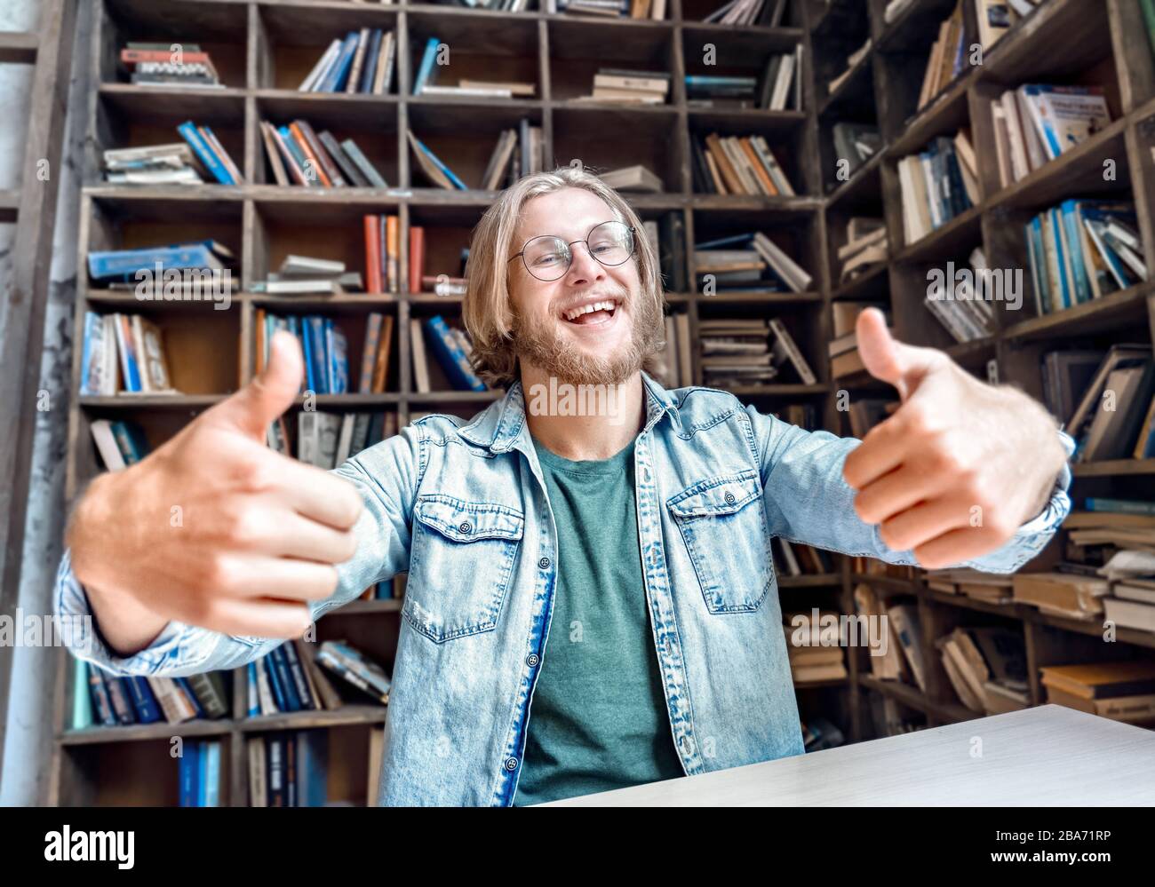 Giovane barbuto sorridente studente blogger guardare fotocamera pollici in su. Foto Stock