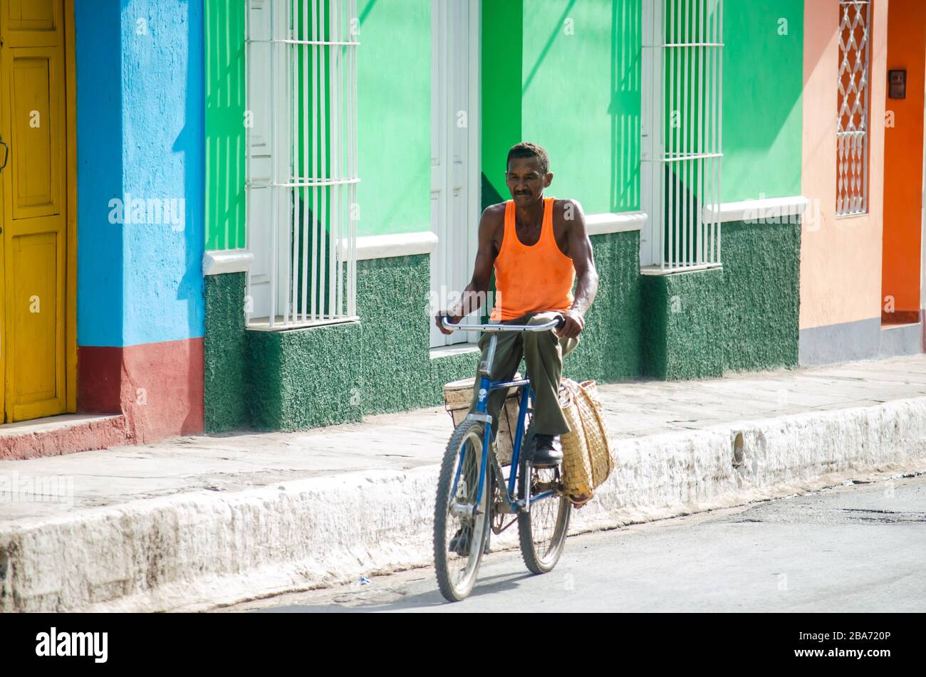 Un uomo che guida una bicicletta per le strade di Trinidad a Cuba, portando una borsa di shopping di paglia di palme come è abituato Foto Stock