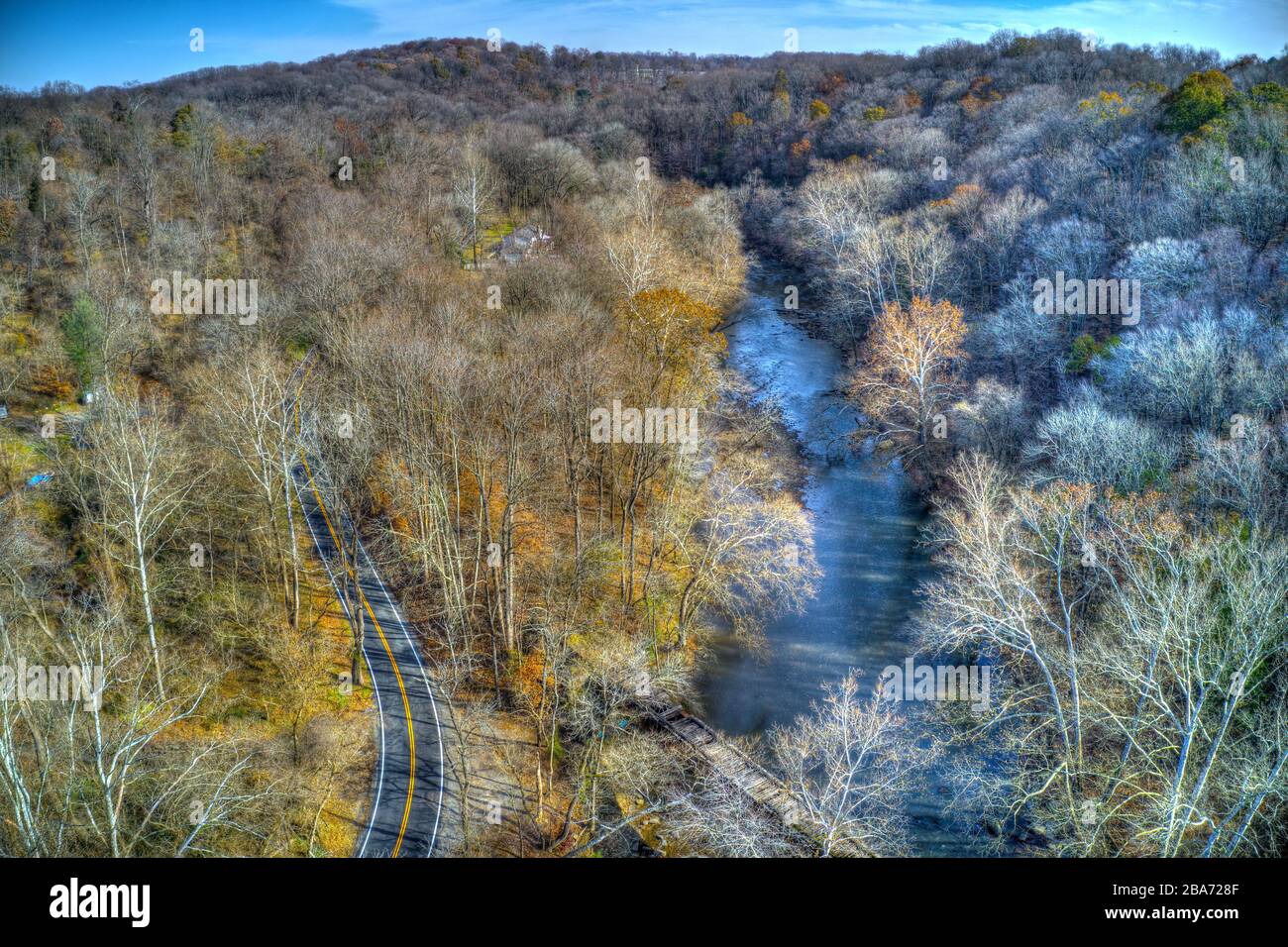 Vista aerea dei boschi nei colori autunnali con una strada, un torrente e una casa Foto Stock