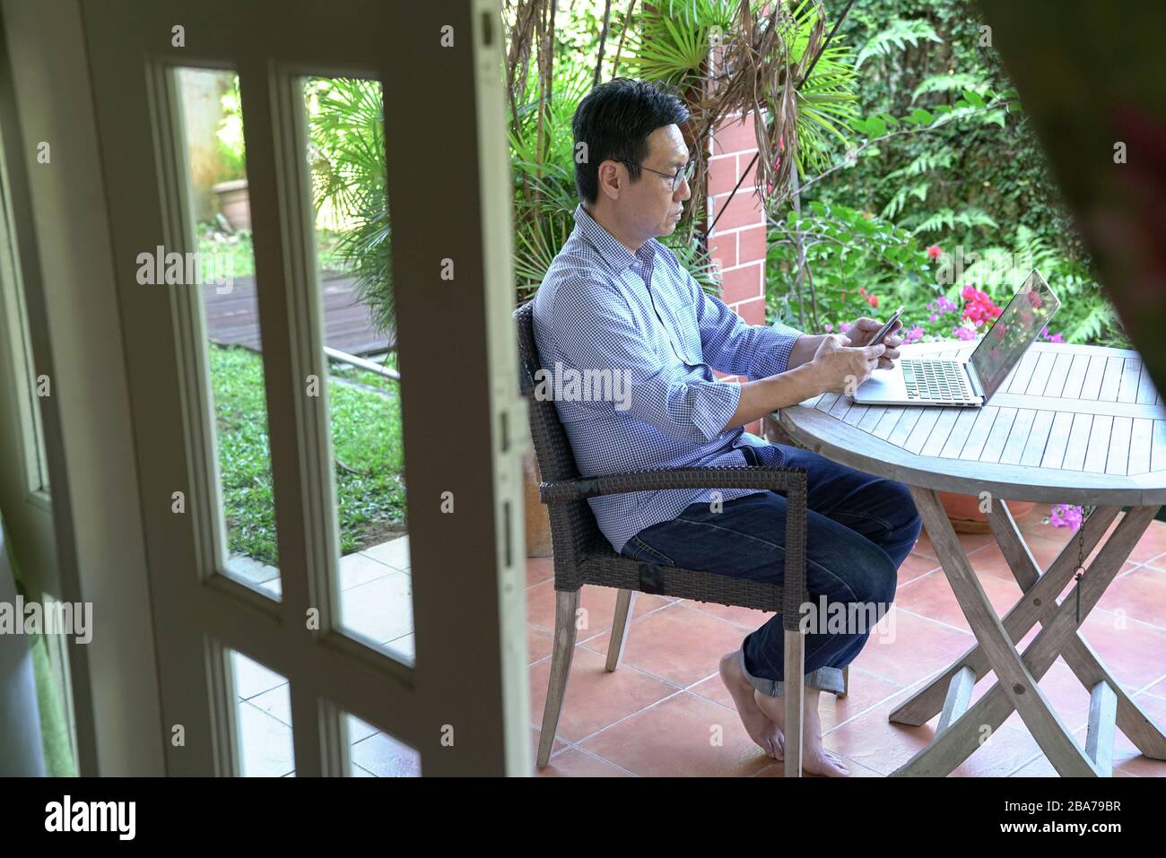 Concetto di lavoro da casa. Messaging cinese asiatico del businessman con il suo telefono delle cellule. Giardino sfondo. Foto Stock