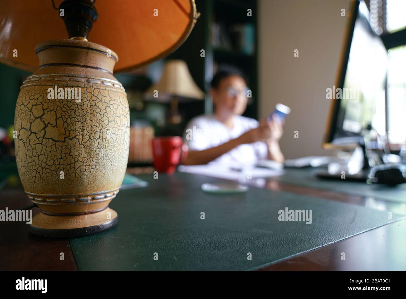 Concetto di lavoro da casa. Concentrati sulla lampada da tavolo con sfondo casa sfocato e uomo sul telefono cellulare. Foto Stock