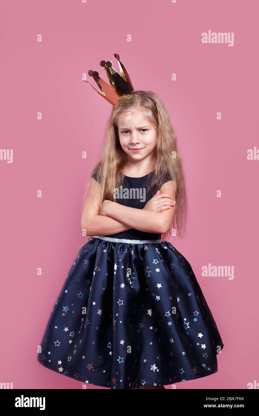 bella ragazza vestita come una piccola principessa incrocia le mani attraverso il petto su sfondo rosa Foto Stock