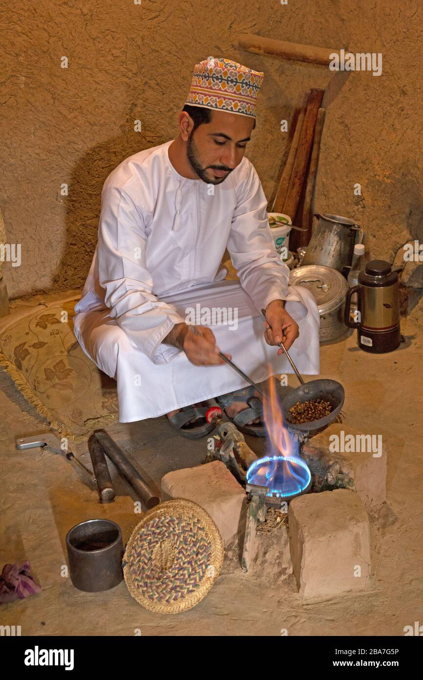 Un uomo Omani in abito tradizionale Omani, tostare i chicchi di caffè in modo tradizionale. Foto Stock