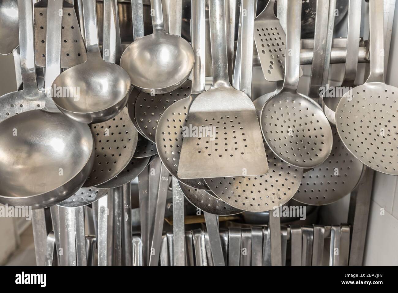Un sacco di cucchiai da cucina appesi in una cucina professionale di un servizio di catering. Foto Stock