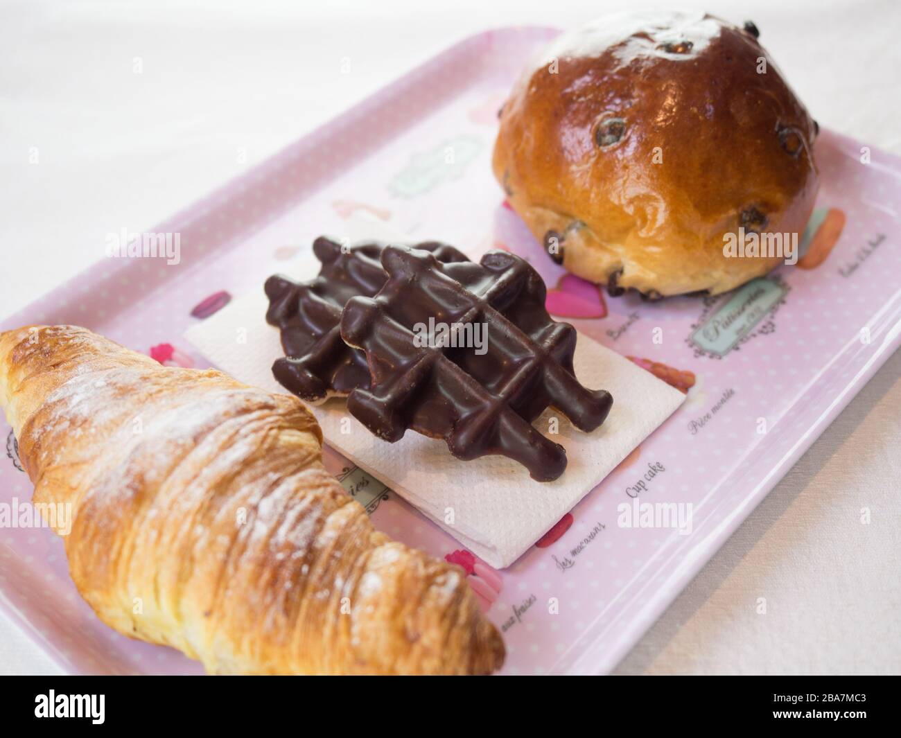 Croissant, waffle al cioccolato e patatine di cioccolato su un piatto rosa Foto Stock