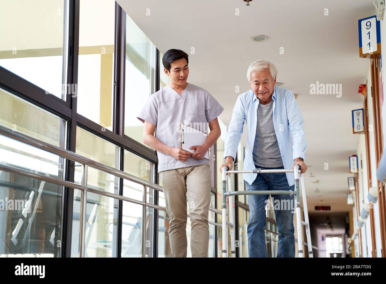 giovane fisioterapista asiatica che lavora con l'uomo anziano a camminare usando un camminatore Foto Stock