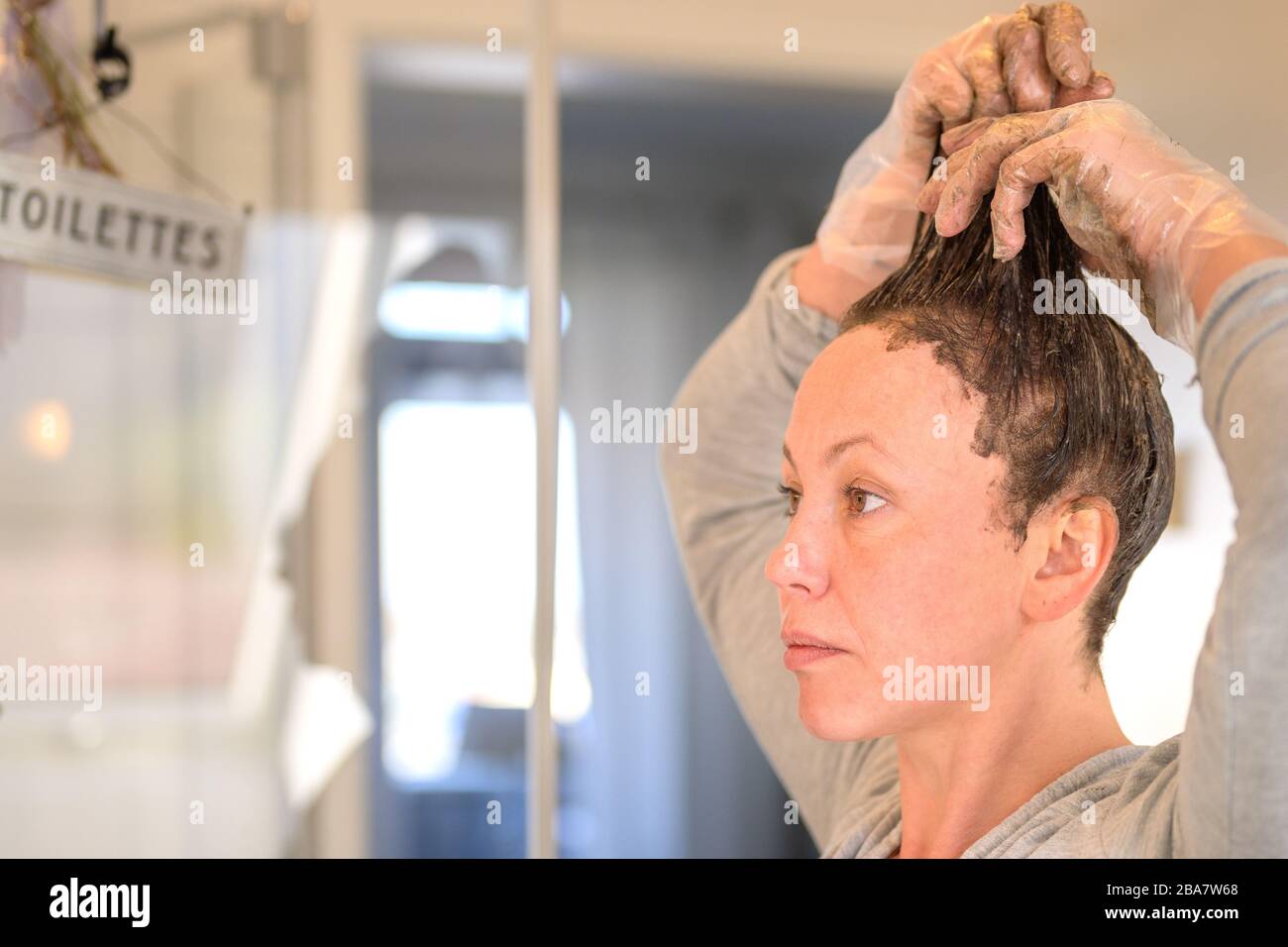 Donna in esecuzione tintura capelli attraverso le punte dei suoi capelli marroni come lei applica il colorante in una vista ravvicinata a casa Foto Stock