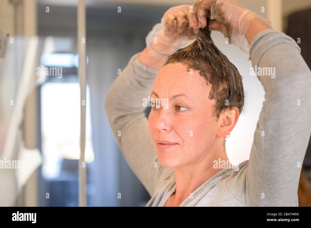 Donna in esecuzione tintura capelli attraverso le punte dei suoi capelli marroni come lei applica il colorante in una vista ravvicinata a casa Foto Stock