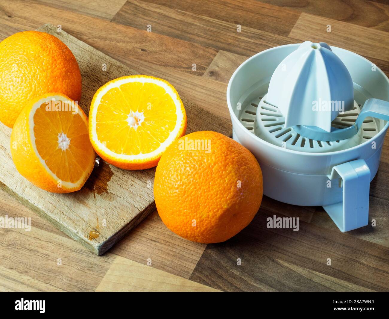 Arance e un arancio dimezzato con un tagliere e uno spremiagrumi su un piano di lavoro da cucina a blocchi di legno Foto Stock