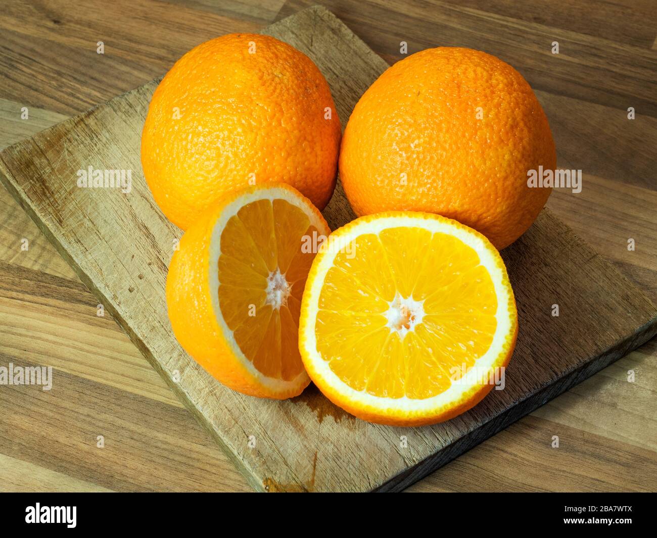 Due arance e un arancio dimezzato su un tagliere su un piano di lavoro da cucina a blocchi di legno Foto Stock