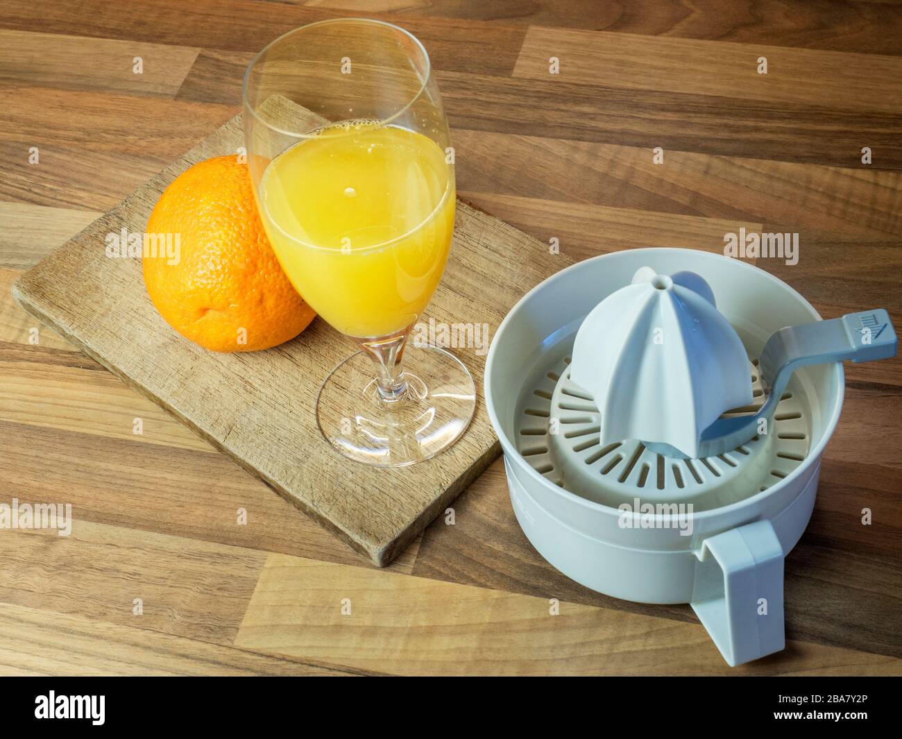 Spremuta d'arancia fresca con un'arancia intera su un tagliere e una spremuta d'arancia su un piano di lavoro della cucina a blocchi di legno Foto Stock