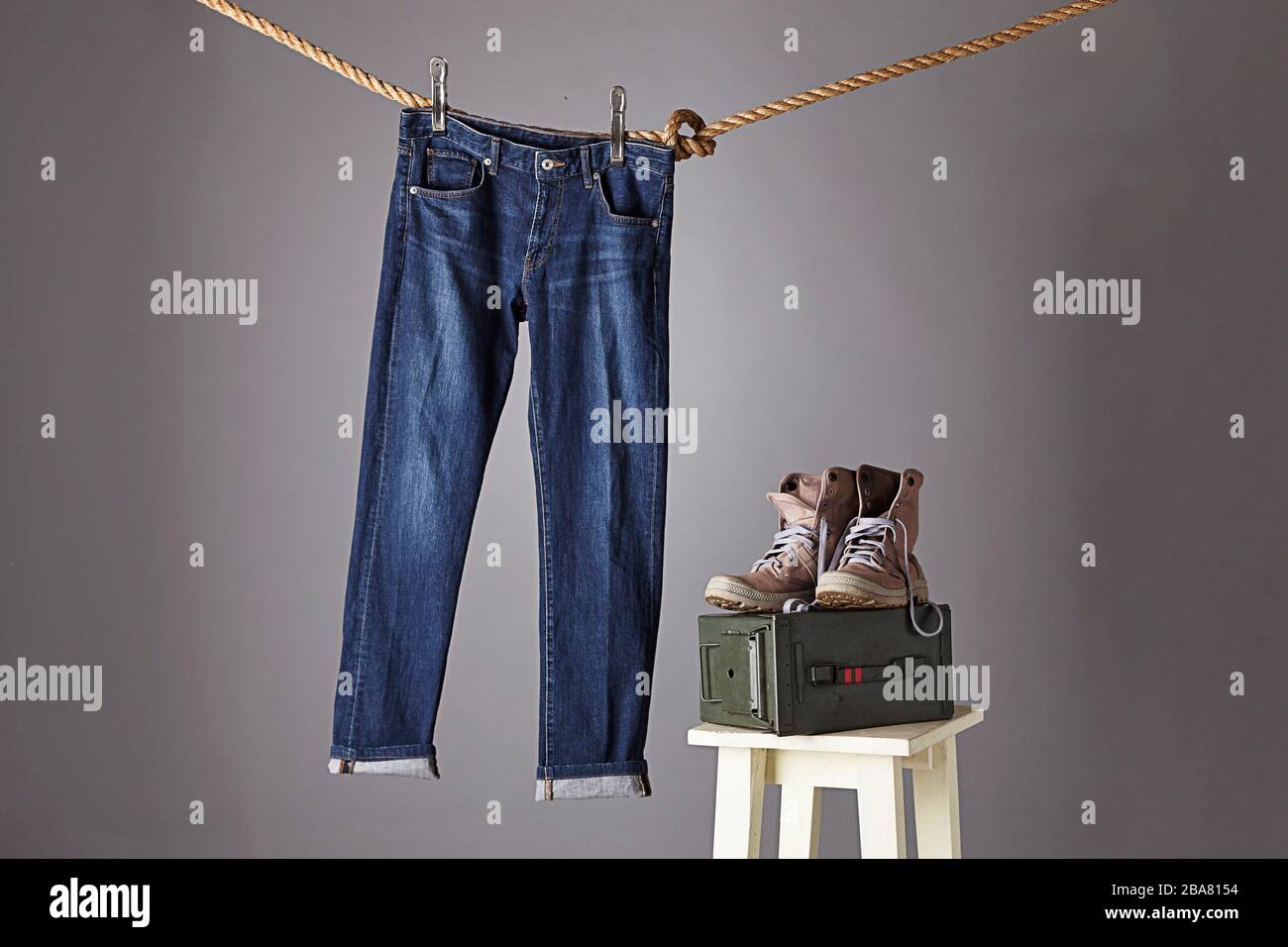 Un jeans blu appeso su una corda con un paio di stivali sulla parte superiore di una scatola di proiettili Foto Stock