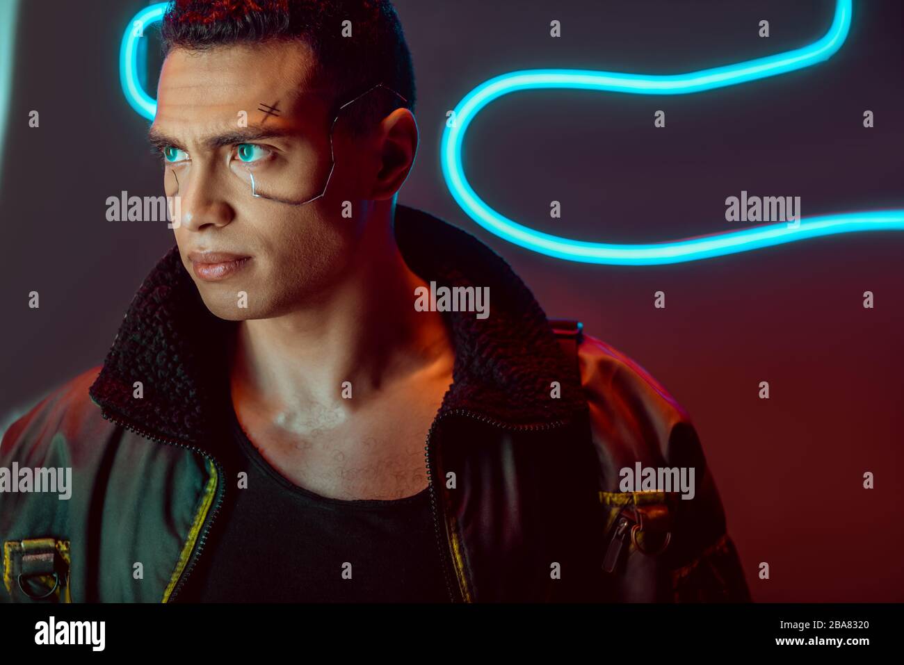 bel giocatore di cyberpunk birazziale che guarda lontano vicino all'illuminazione al neon su nero Foto Stock