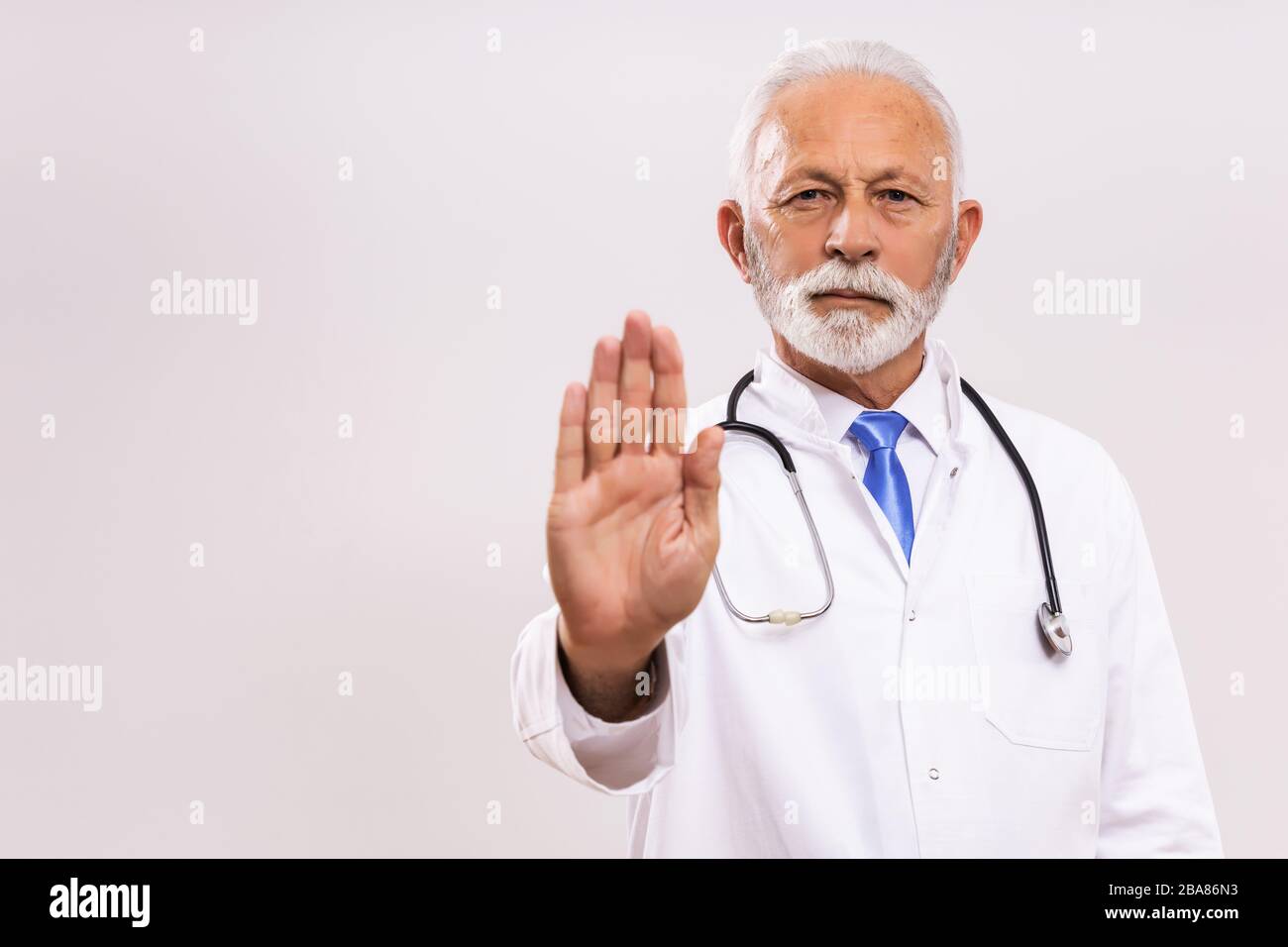 Ritratto del medico senior che mostra il segnale di stop su sfondo grigio. Foto Stock