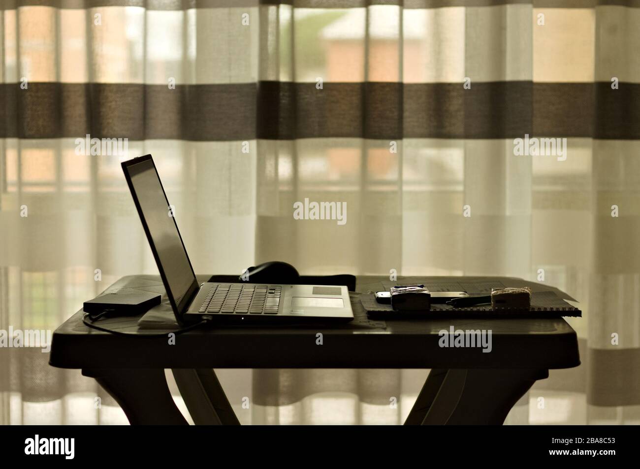 Lavoro intelligente: Postazione di lavoro con notebook nel soggiorno di fronte a una tenda a strisce (Italia, Europa) Foto Stock