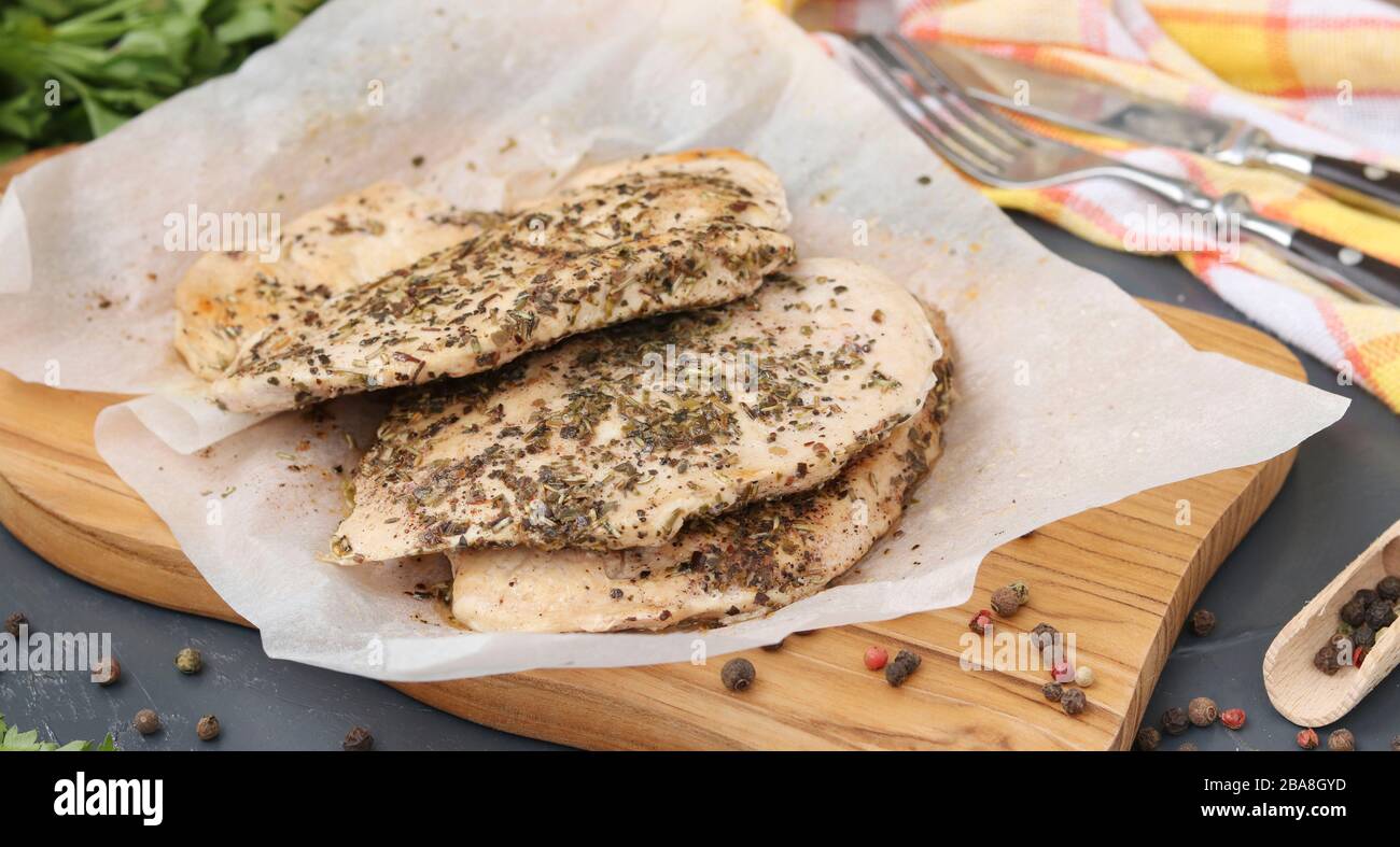 Filetto di pollo con erbe aromatiche su pergamena su un asse di legno, sana alimentazione Foto Stock