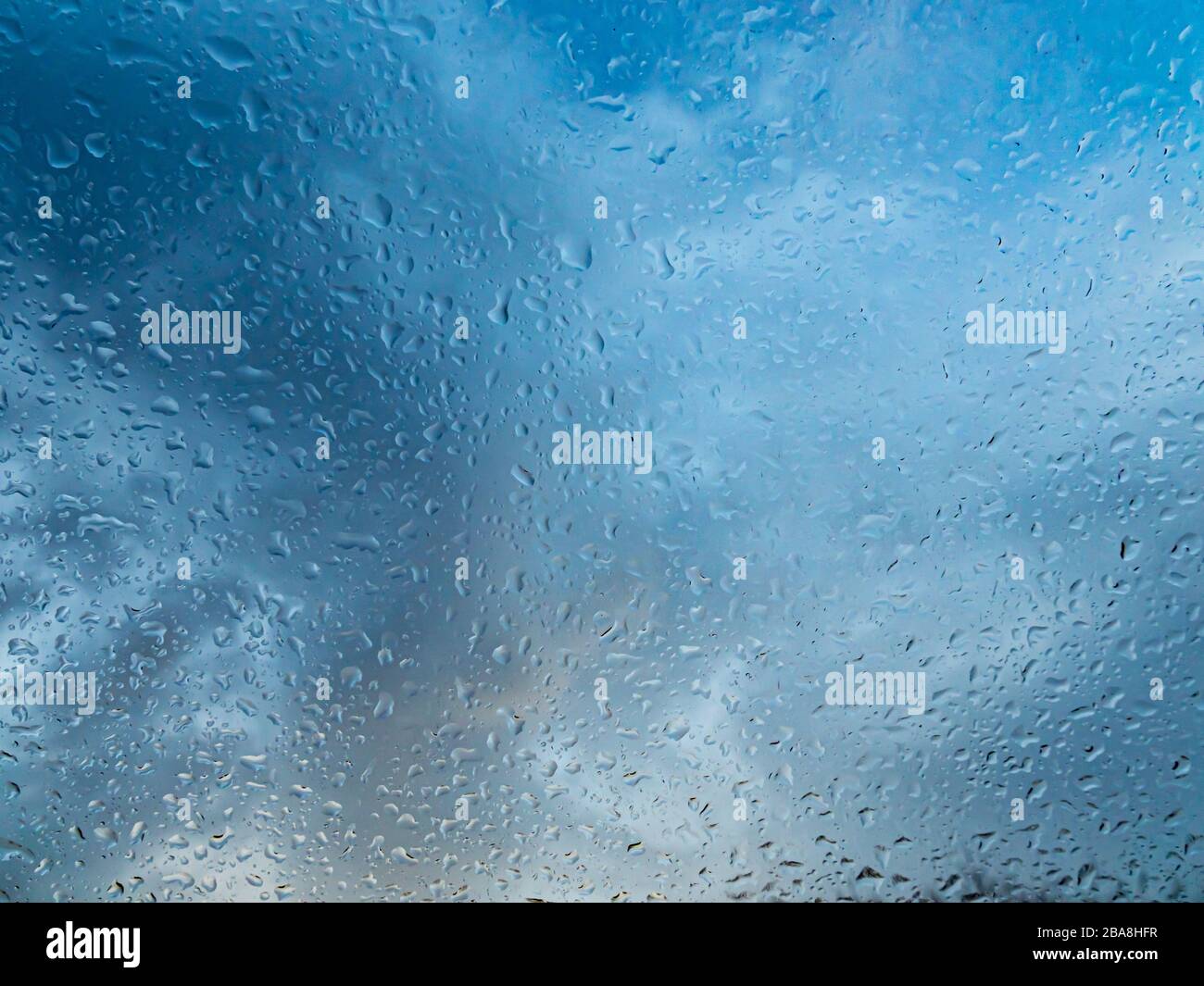 Finestra bagnata con gocce di pioggia e un cielo nuvoloso su sfondo. Foto Stock