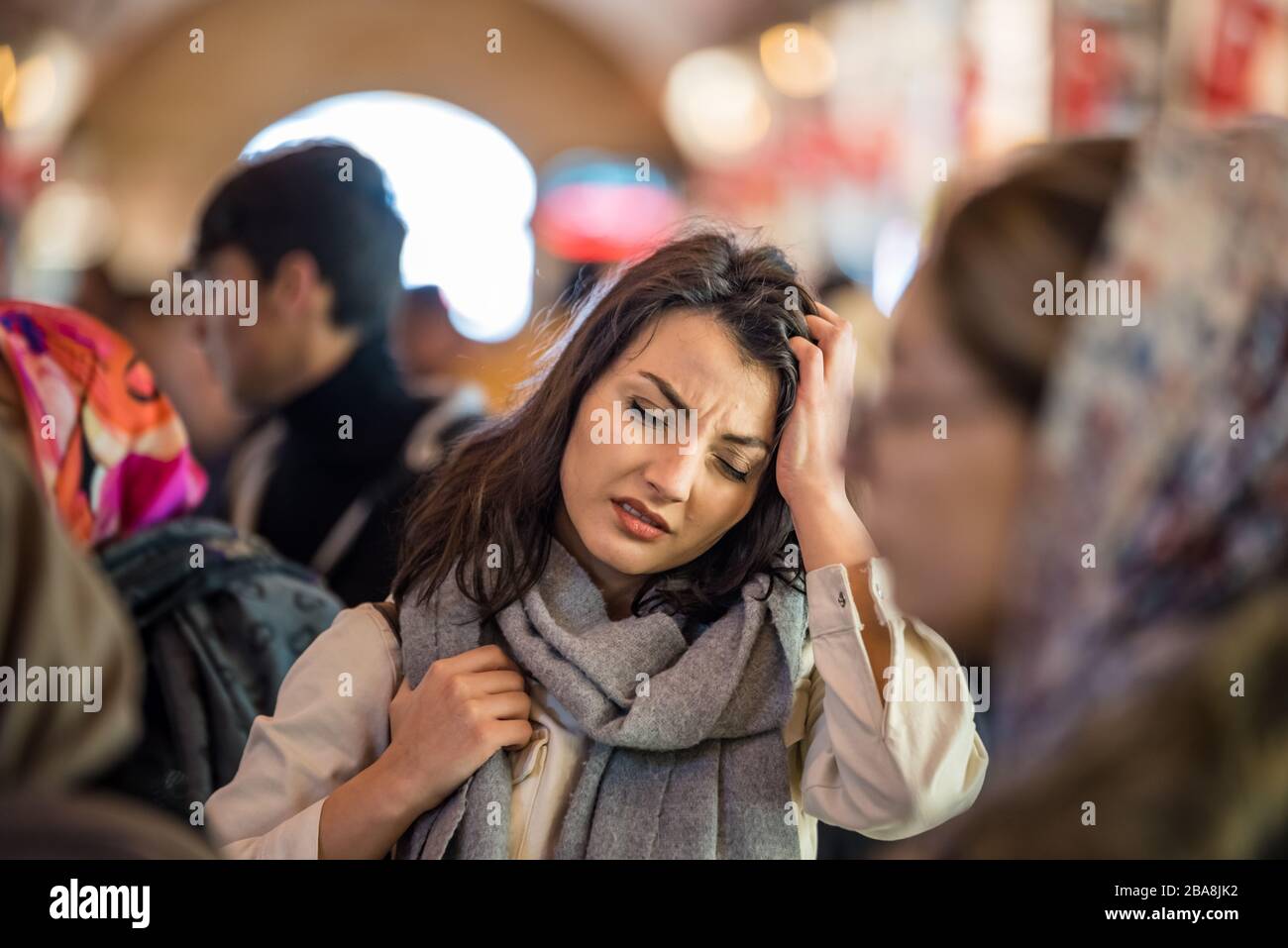 Bella donna in abiti moderni alla moda soffre emicrania o mal di testa problema mentre in piedi folla di persone in strada. Foto Stock