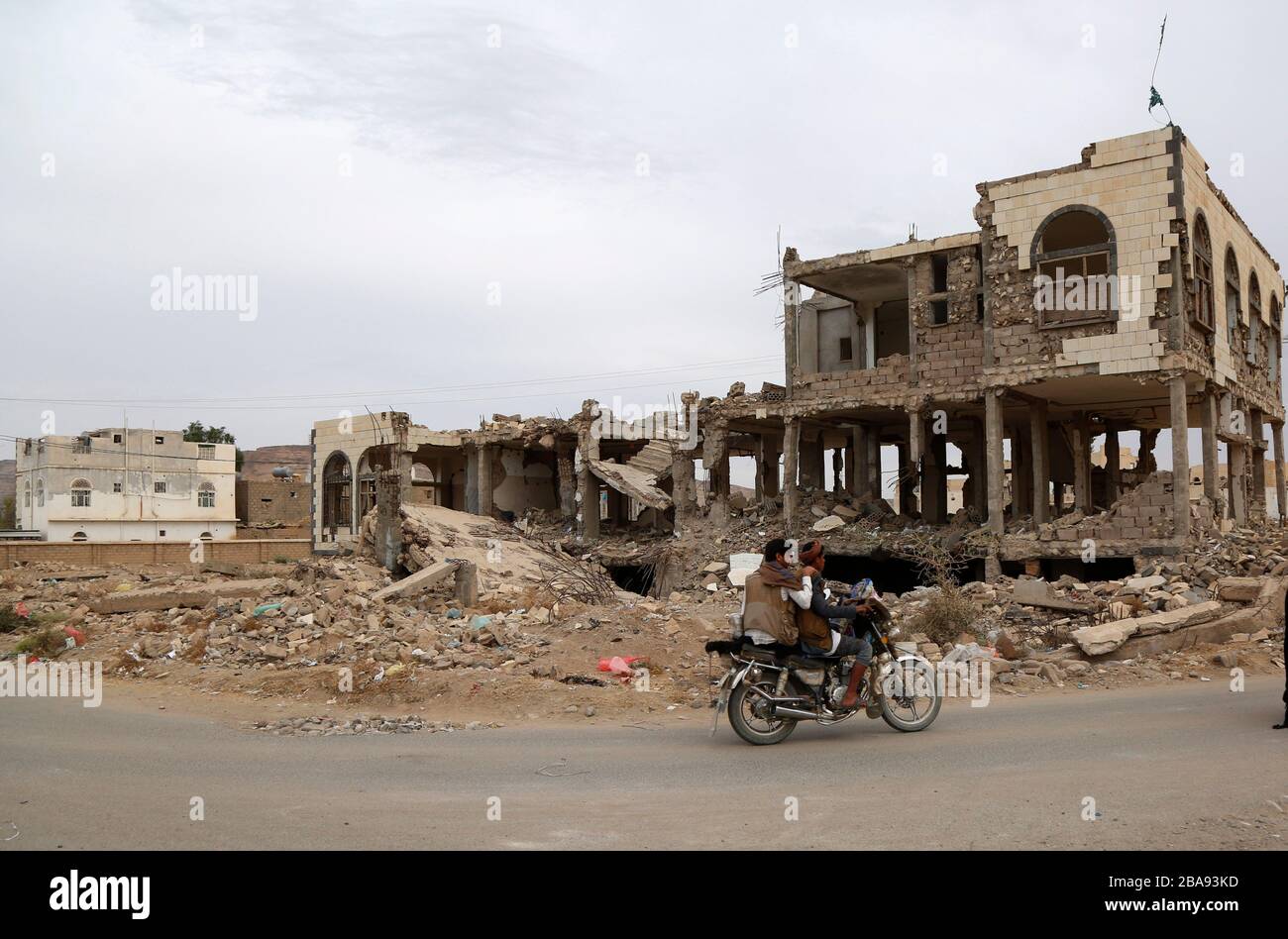 Saada, Yemen. 19 Mar 2020. Gli uomini cavalcano una motocicletta vicino a una casa distrutta dagli attacchi aerei durante la guerra in corso nella provincia di Saada, Yemen, 19 marzo 2020. PER ANDARE CON 'caratteristica: La guerra dello Yemen entra il 6 ° anno senza fine in vista' Credit: Mohammed Mohammed/Xinhua/Alamy Live News Foto Stock