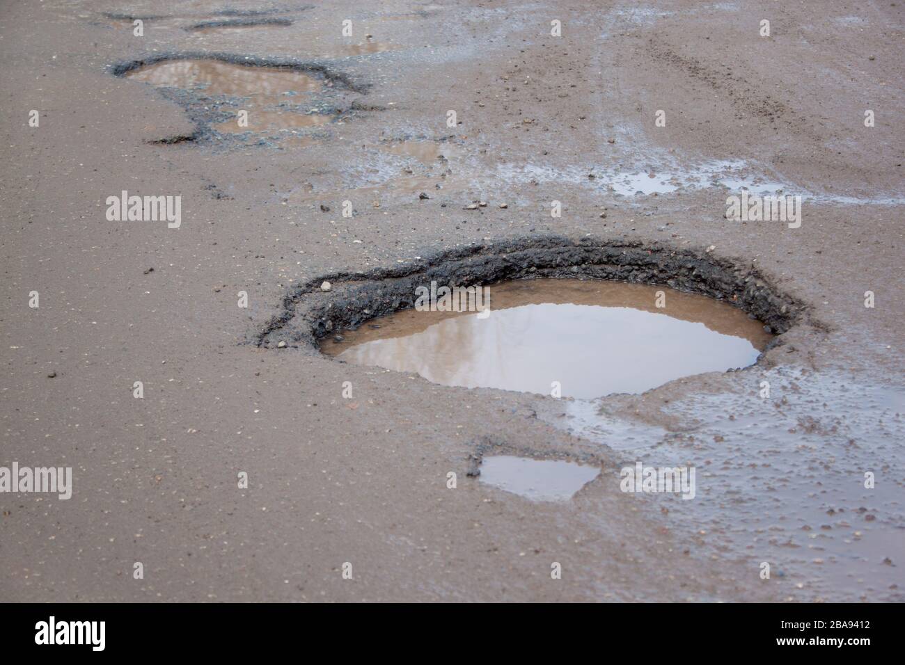 La cattiva strada asfaltata con una grande buche piena d'acqua. Pericoloso distrutto su strada. Riflessi specchio nell'acqua. Foto Stock