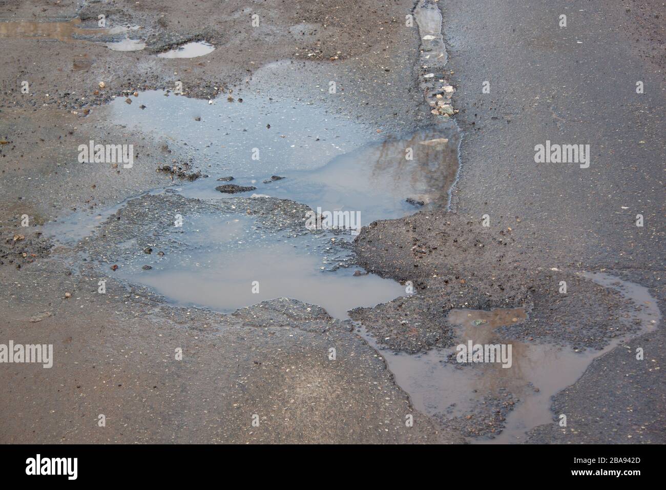 La cattiva strada asfaltata con una buche piena d'acqua. Pericoloso distrutto su strada. Acqua limpida nella pozzanghera. Foto Stock