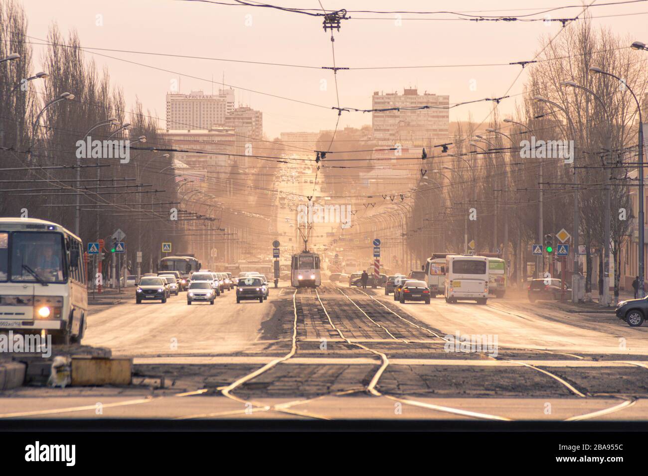 traffico in città strada diversi veicoli si muovono, così come il trasporto elettrico ferrovia e alberi stradali sono a sinistra senza foglie ai bordi della strada, hotell - Foto Stock