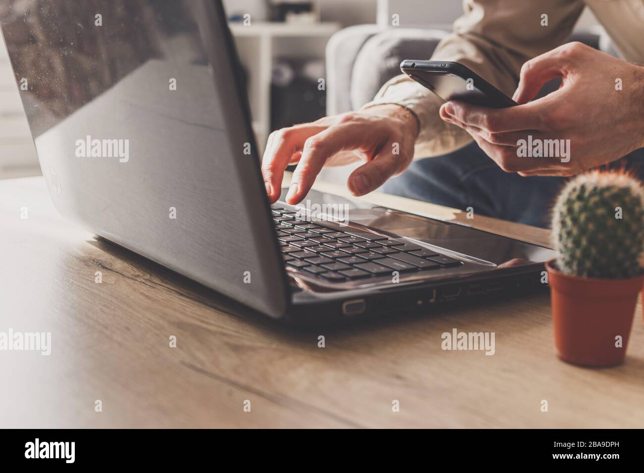 Primo piano di un uomo d'affari che lavora su computer portatile e smartphone, inviando e-mail da casa Foto Stock