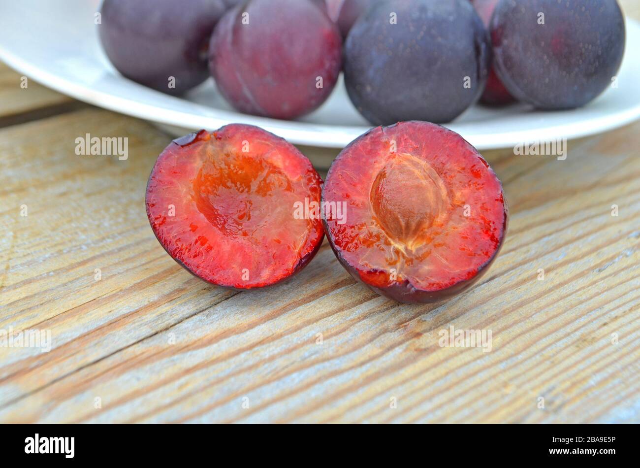 Primo piano di prugne a fette mature in una ciotola, fuoco selettivo. Prugne fresche su tavola di legno Foto Stock