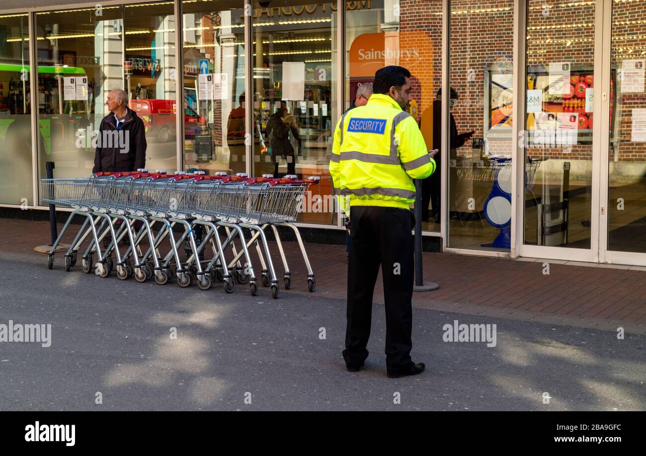 Winchester, Hampshire, Inghilterra, Regno Unito, marzo 2020. Responsabile della sicurezza fuori da un supermercato Winchester. Consentire l'immissione di un solo cliente alla volta Foto Stock