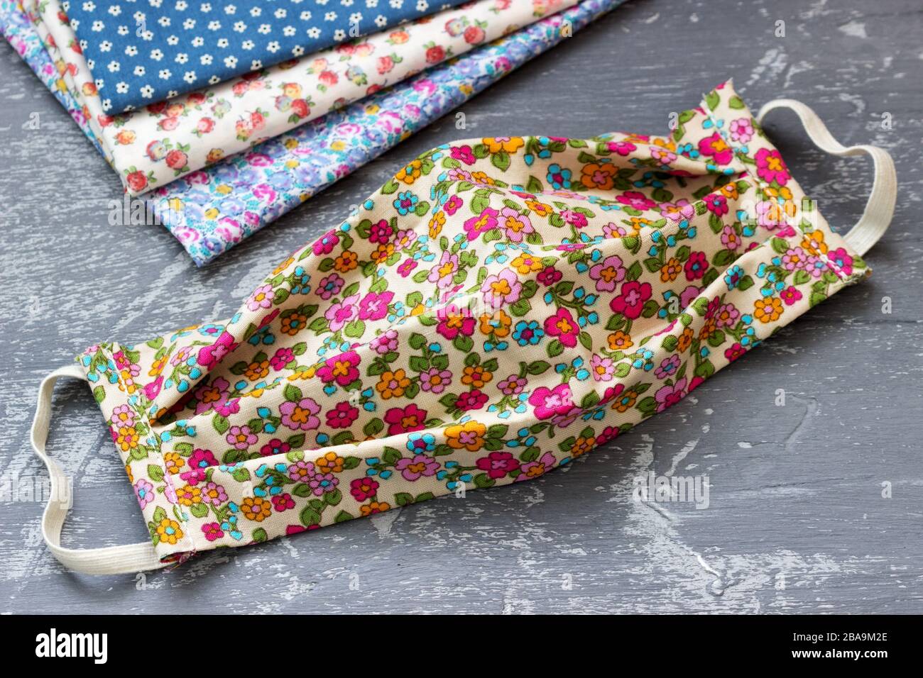 Maschera protettiva fatta in casa e pezzi di stoffa su sfondo grigio. Foto Stock