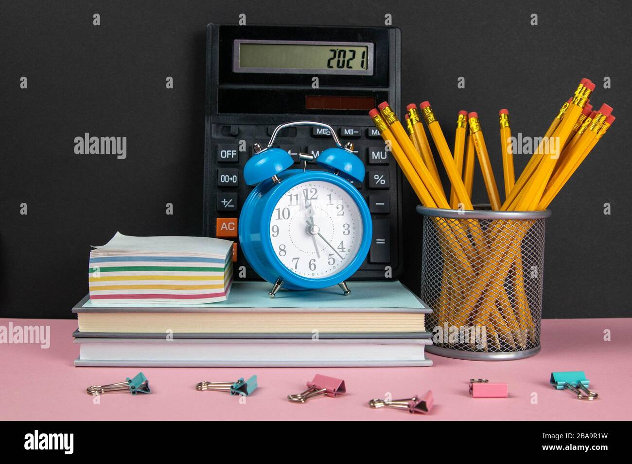 Su una pila di libri c'è una calcolatrice, un orologio e fogli per le note, e accanto ad un bicchiere di matite Foto Stock
