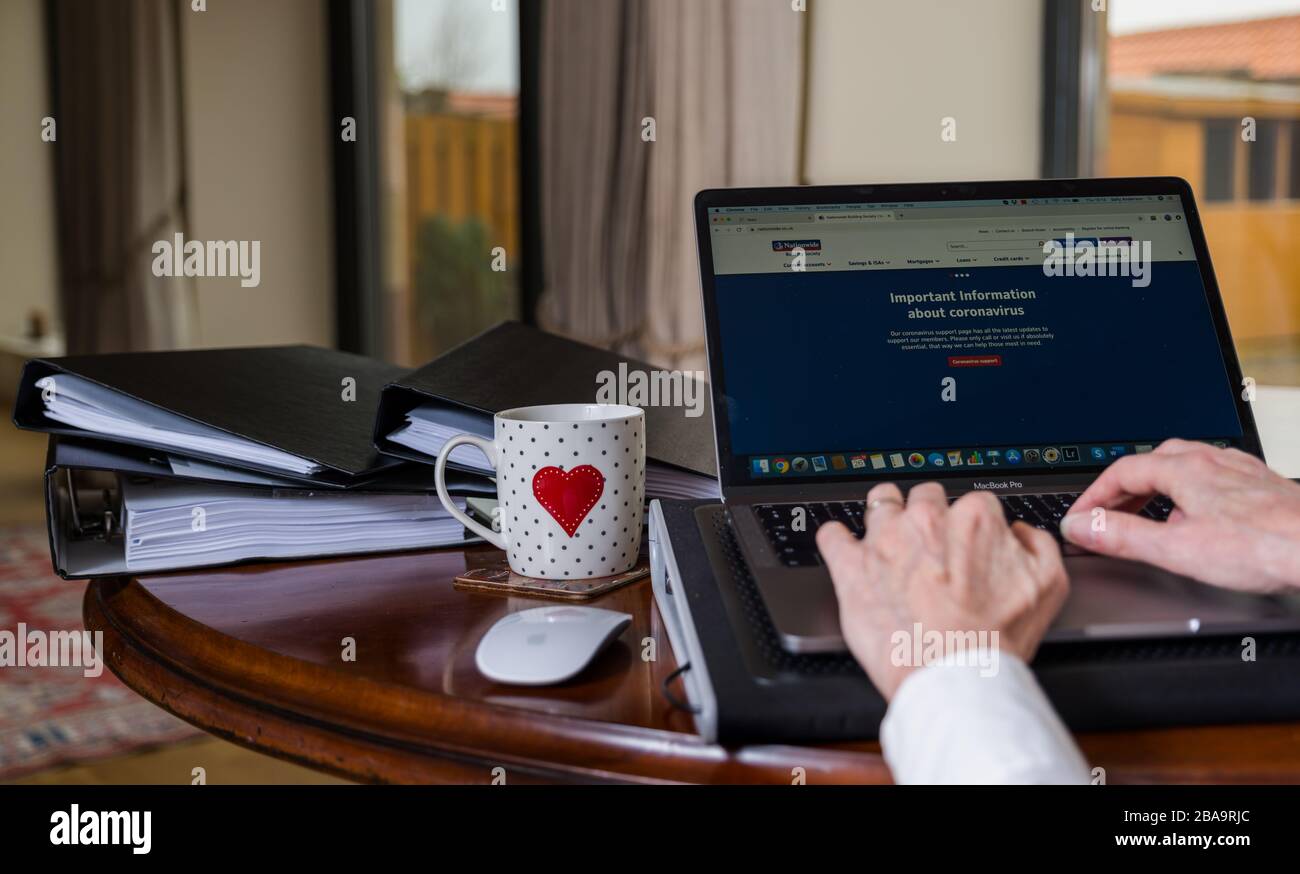 Donna che lavora su un computer portatile a casa con schermo che mostra il sito Web della Società di costruzione nazionale con informazioni su Coronavirus Covid-19 Foto Stock