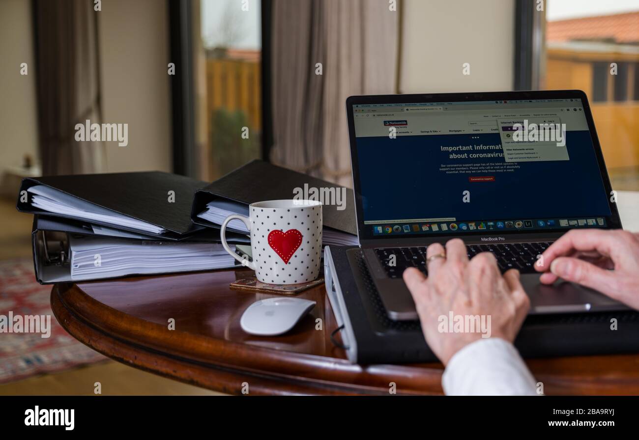 Donna che lavora su un computer portatile a casa con schermo che mostra il sito Web della Società di costruzione nazionale con informazioni su Coronavirus Covid-19 Foto Stock