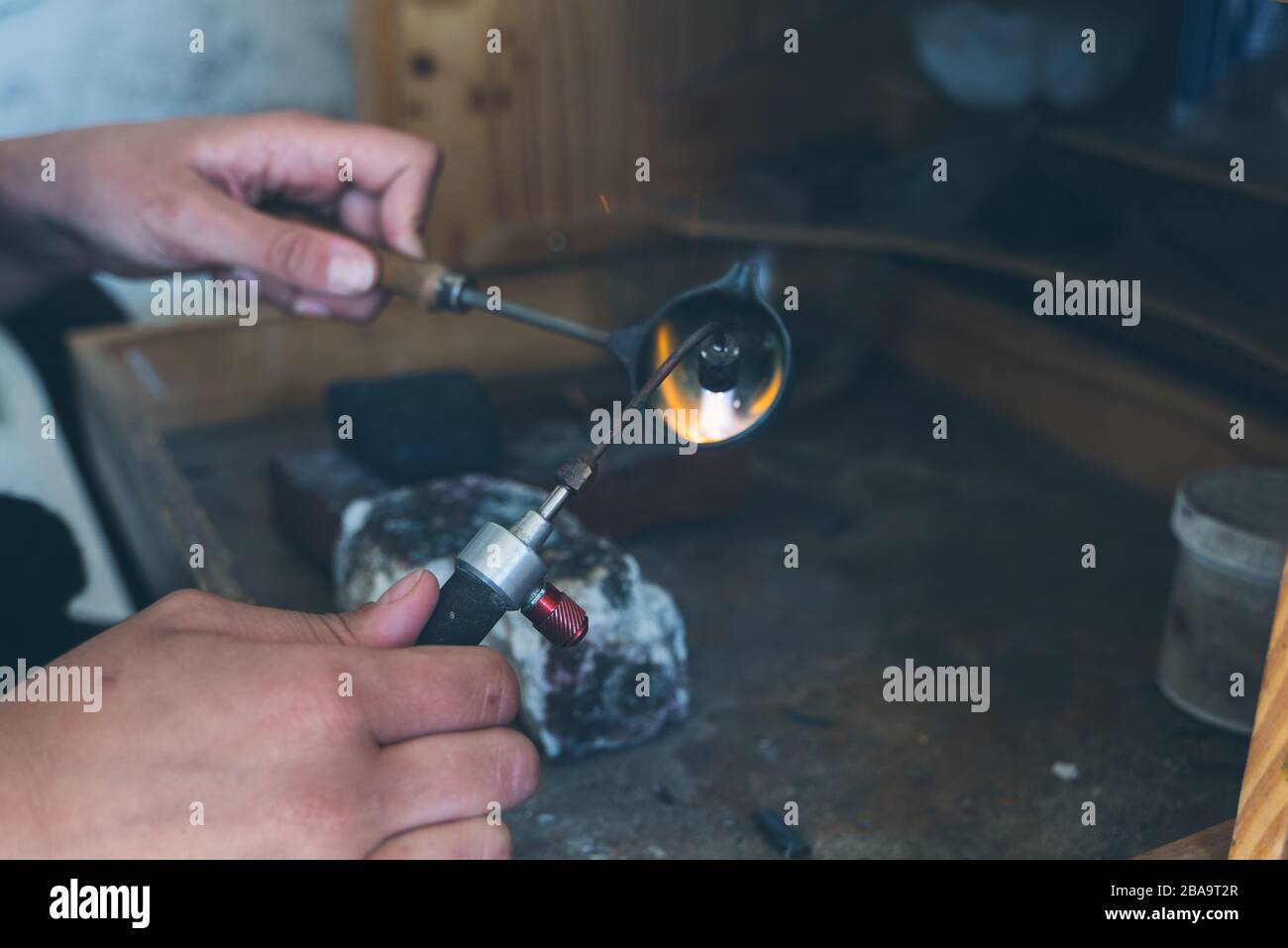 Dettaglio delle mani con cannello per fondere metallo fine durante la lavorazione Foto Stock