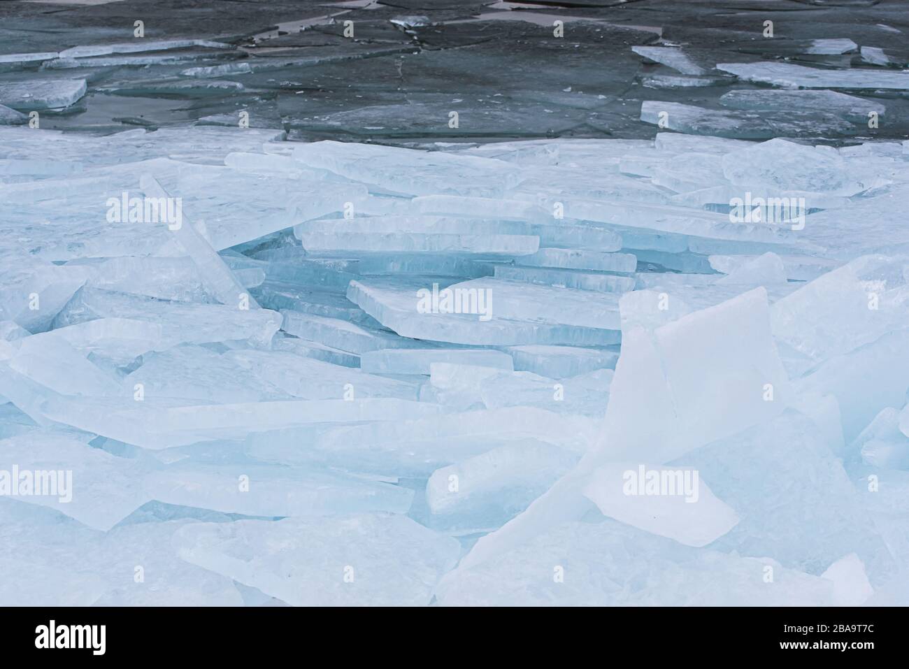 Grandi pezzi di ghiaccio pianeggianti si accumulano lungo la riva di un lago in inverno. Foto Stock