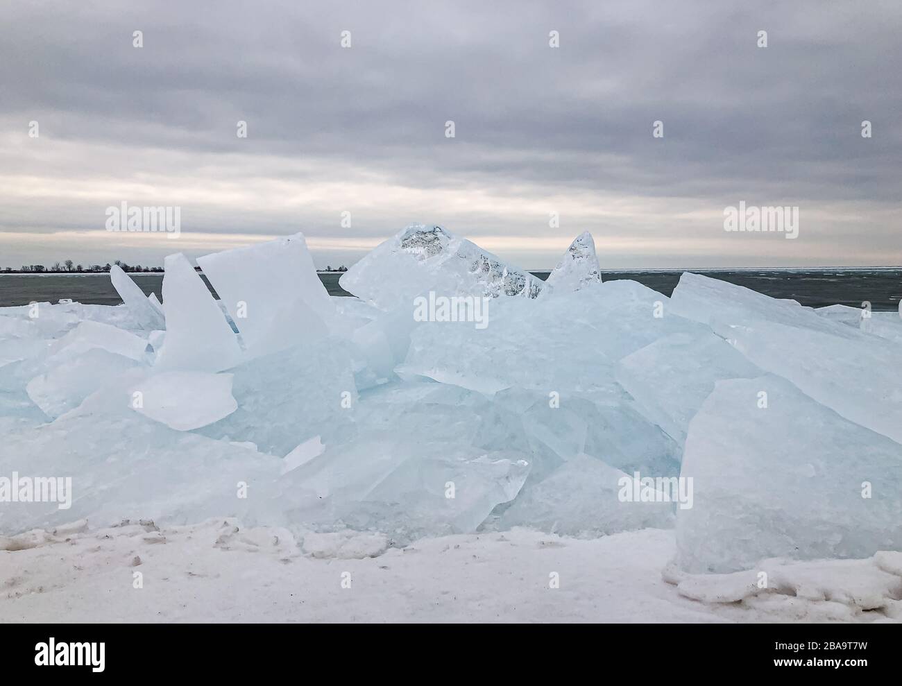 Grandi pezzi di ghiaccio pianeggianti si accumulano lungo la riva di un lago in inverno. Foto Stock