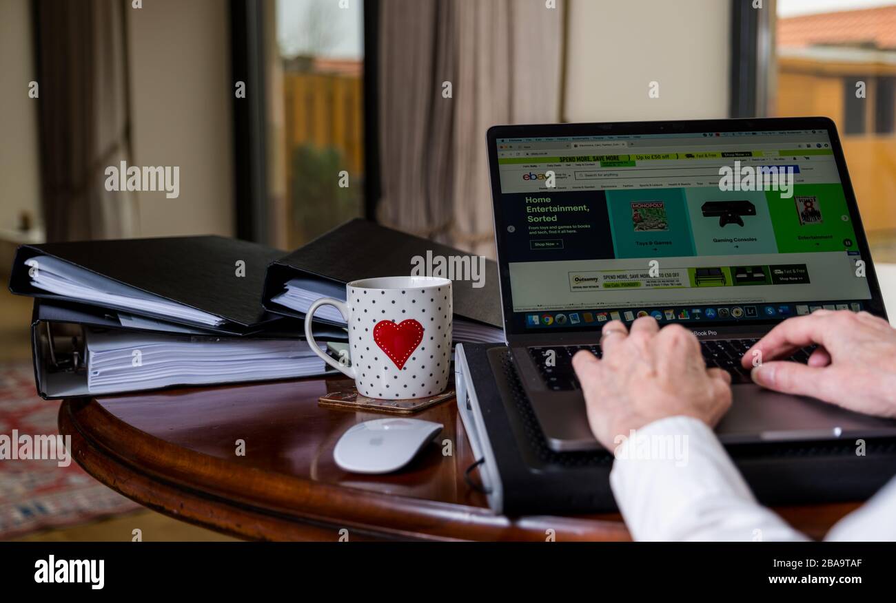 Donna che lavora su un laptop sul tavolo a casa con schermo che mostra la pagina di eBay online shopping sito web Foto Stock