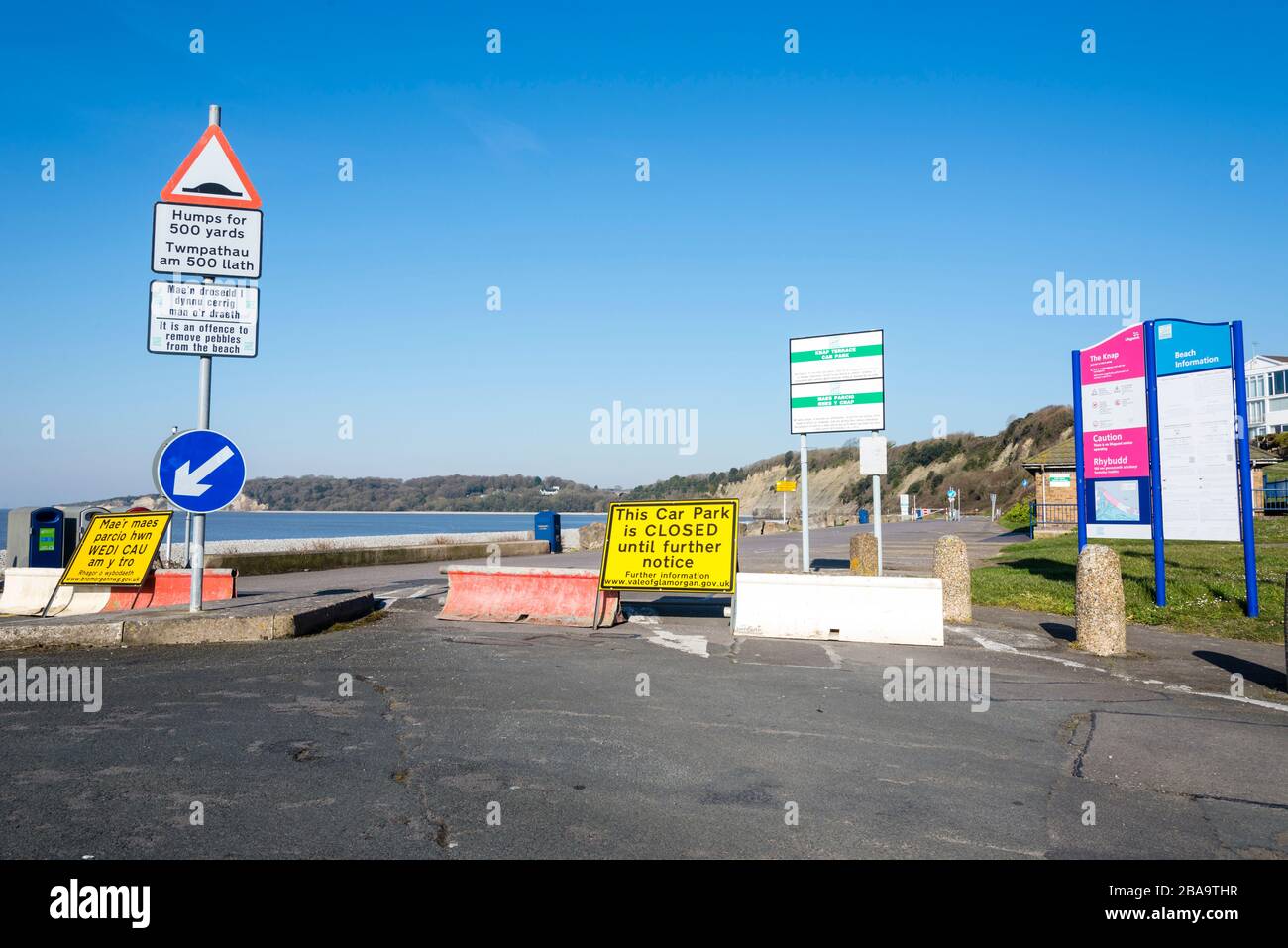 In una giornata di sole l'ingresso a un parcheggio sul mare è bloccato da una barriera temporanea durante le crisi di coronavirus. Indicazioni in lingua gallese e inglese Foto Stock